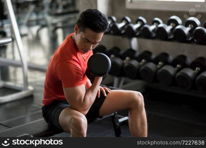 Muscle Asian handsome bodybuilder exercise biceps with heavy dumbbells near ftiness gym shelf. Muscular body sportsman in sport fitness center. Bodybuilding and healthy lifestyle.