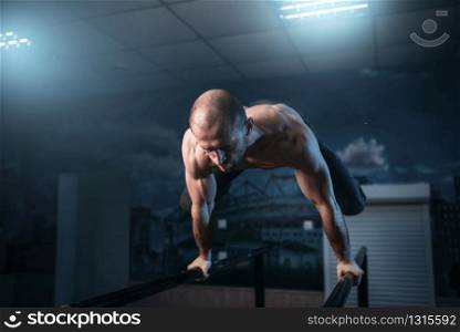 Muscle athlete makes horizontal balance exercises on gymnastic bars in gym. Strong gymnast on training. Horizontal balance exercises on gymnastic bars
