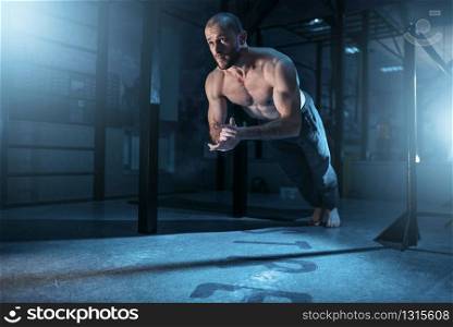 Muscle athlete makes pushups exercises in gym. Strong gymnast on training