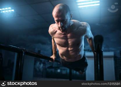 Muscle gymnast exercises on sports bars in gym. Strong athlete on gymnastic training