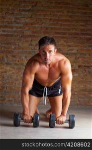 muscle shaped man on knees with training weights on brickwall