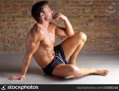 muscle shaped man sitting relaxed on grunge brickwall