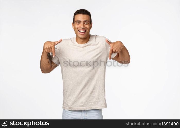 Muscline good-looking tanned strong man in casual t-shirt, pointing down, smiling satisfied and happy, sharing interesting link, recommend use product, advertise new application, white background.. Muscline good-looking tanned strong man in casual t-shirt, pointing down, smiling satisfied and happy, sharing interesting link, recommend use product, advertise new application, white background