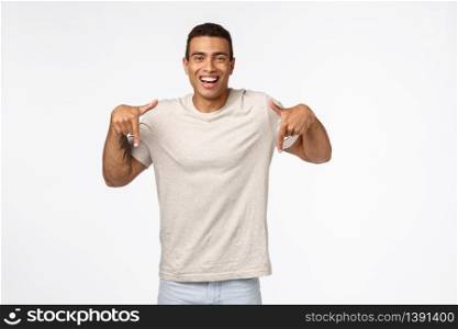 Muscline good-looking tanned strong man in casual t-shirt, pointing down, smiling satisfied and happy, sharing interesting link, recommend use product, advertise new application, white background.. Muscline good-looking tanned strong man in casual t-shirt, pointing down, smiling satisfied and happy, sharing interesting link, recommend use product, advertise new application, white background