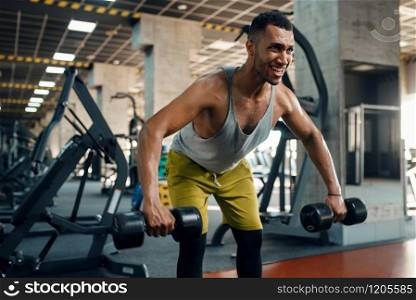 Muscular athlete in sportswear doing exercise with dumbbells on training in gym. Workout in sport club, healthy lifestyle. Athlete doing exercise with dumbbells in gym