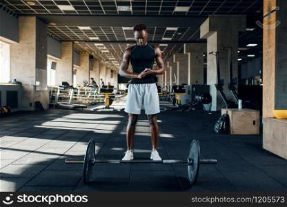 Muscular athlete in sportswear prepares for exercise with barbell on training in gym. Workout in sport club, healthy lifestyle