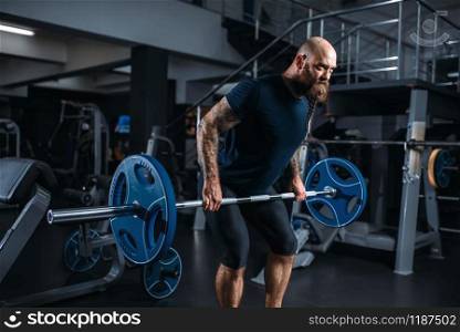 Muscular athlete in sportswear takes weight, training in gym. Bearded man on workout in sport club, healthy lifestyle. Muscular athlete in sportswear takes weight