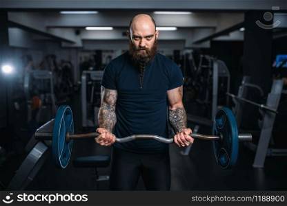 Muscular athlete in sportswear takes weight, training in gym. Bearded man on workout in sport club. Muscular athlete in sportswear takes weight