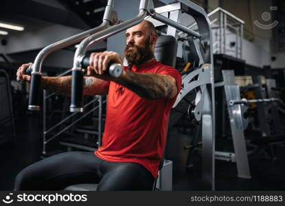 Muscular athlete on exercise machine in gym. Bearded man on workout in sport club, healthy lifestyle