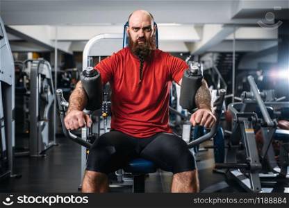 Muscular athlete on exercise machine in gym. Bearded man on workout in sport club, healthy lifestyle. Muscular athlete on exercise machine in gym