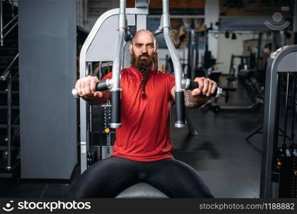 Muscular athlete on exercise machine in gym. Bearded man on workout in sport club. Muscular athlete on exercise machine in gym