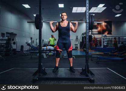 Muscular athlete prepares to make squats with barbell in gym. Weightlifting workout, powerlifting training