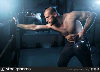 Muscular athlete workout, man lifting kettlebell. Strong sportsman training with weight