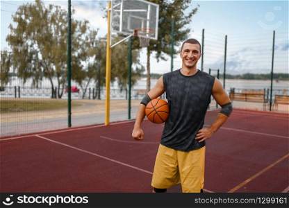 Muscular basketball player on outdoor court. Male athlete in sportswear holds ball on streetball training