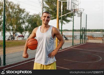 Muscular basketball player on outdoor court. Male athlete in sportswear holds ball on streetball training. Muscular basketball player on outdoor court