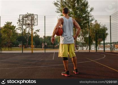Muscular basketball player on outdoor court. Male athlete in sportswear holds ball on streetball training. Muscular basketball player on outdoor court