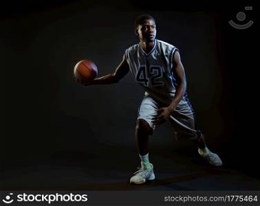 Muscular basketball player with ball shows his skill in studio, black background. Professional male baller in sportswear playing sport game, tall sportsman. Muscular basketball player, black background