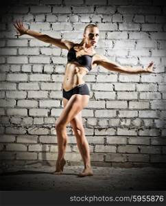 Muscular dancing woman on grey brick wall (dark version)