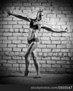 Muscular dancing woman on grey brick wall (monochrome version)