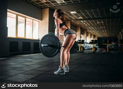 Muscular female athlete training with barbell in sport gym. Woman exercise with weight in fitness club. Female athlete training with barbell in sport gym