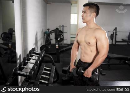Muscular fitness man bodybuilder is workout with dumbbells in gym