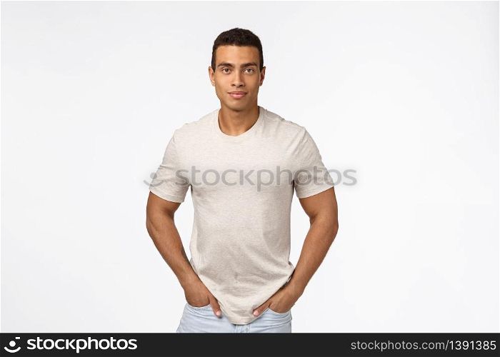 Muscular handsome hispanic man with short haircut, strong biceps, hold hands in jeans pockets and smiling camera, standing casually over white background, trustworthy, sincere expression.. Muscular handsome hispanic man with short haircut, strong biceps, hold hands in jeans pockets and smiling camera, standing casually over white background, trustworthy, sincere expression