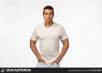 Muscular handsome hispanic man with short haircut, strong biceps, hold hands in jeans pockets and smiling camera, standing casually over white background, trustworthy, sincere expression.. Muscular handsome hispanic man with short haircut, strong biceps, hold hands in jeans pockets and smiling camera, standing casually over white background, trustworthy, sincere expression