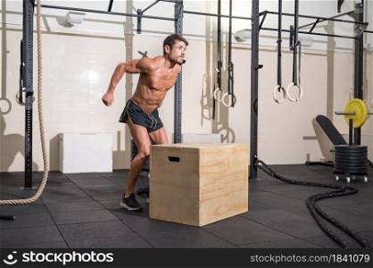 Muscular male athlete is practicing jumping on a wooden box in modern health club. Functional training. High quality photo. Muscular male athlete is practicing jumping on a wooden box in modern health club. Functional training