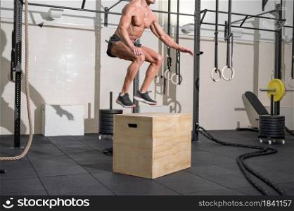 Muscular male athlete is practicing jumping on a wooden box in modern health club. Functional training. High quality photo. Muscular male athlete is practicing jumping on a wooden box in modern health club. Functional training