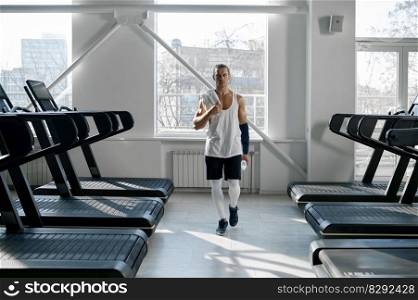 Muscular male bodybuilder having break after cardio. Confident man athlete over treadmills set in gym interior. Muscular male bodybuilder having break after cardio on treadmill machine