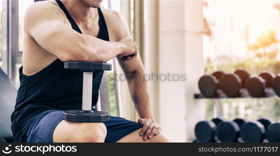 Muscular man bodybuilder in fitness gym training with dumbbells. Healthy lifestyle and bodybuilding concept.