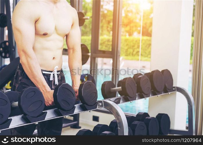 Muscular man bodybuilder in fitness gym training with dumbbells. Healthy lifestyle and bodybuilding concept.. Muscular man bodybuilder training with dumbbells.