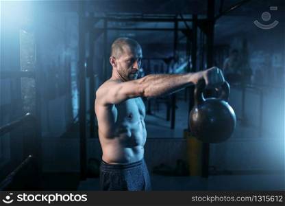 Muscular man exercises with kettlebell on training in gym. Strong athlete workout with weight. Muscular man exercises with kettlebell on training