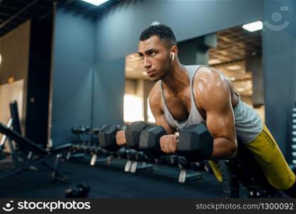 Muscular man in sportswear doing exercise with dumbbells on the bench, training in gym. Workout in sport club, healthy lifestyle. Man doing exercise with dumbbells on the bench