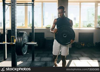 Muscular man in sportswear prepares barbell on training in gym. Workout in sport club, healthy lifestyle. Muscular man in sportswear prepares barbell in gym