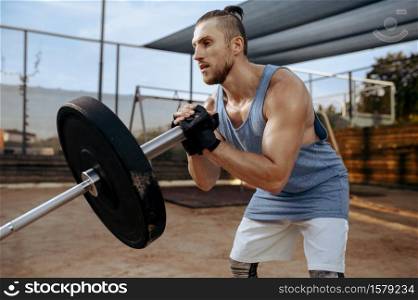 Muscular man prepares barbell weights for exercise, street workout. Fitness training on sports ground outdoor, male person pumps muscles. Man prepares barbell weights, street workout
