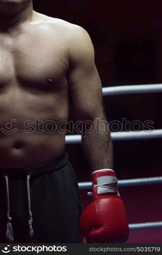 muscular professional kick boxer resting on the ropes in the corner of the ring while training for the next match with a focus on his glove
