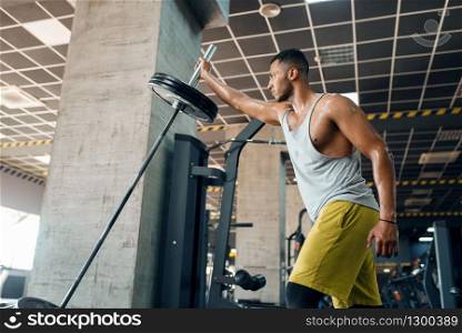 Muscular sporsman in sportswear doing exercise with barbell on training in gym. Workout in sport club, healthy lifestyle. Sporsman doing exercise with barbell in gym