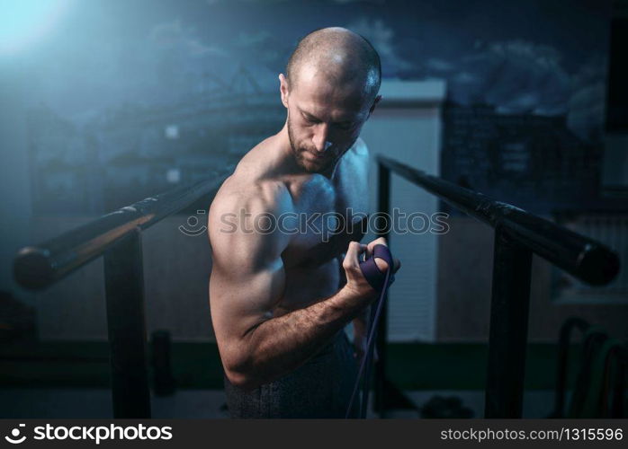 Muscular sports man exercises with elastic rubber band. Active sport lifestyle. Male strong biceps