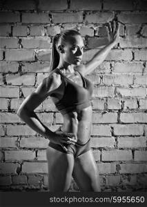 Muscular woman on grey brick wall background (monochrome version)