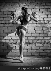 Muscular woman on grey brick wall (monochrome version)