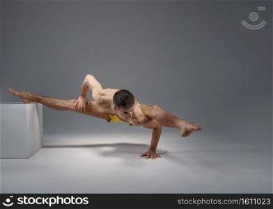 Muscular yoga keeps balanc in difficult pose on the pedestal, meditation position, grey background. Strong man doing yogi exercise, asana training, top concentration, healthy lifestyle. Muscular yoga keeps balanc on the pedestal