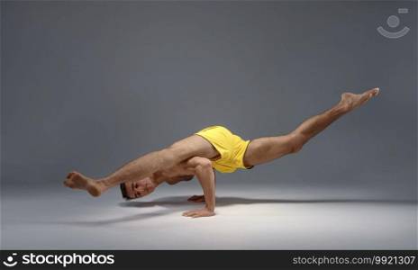 Muscular yoga stands on hands in difficult pose, meditation position, grey background. Strong man doing yogi exercise, asana training, top concentration, healthy lifestyle. Muscular yoga stands on hands in difficult pose