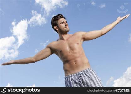 Muscular young man standing arms outstretched against cloudy sky