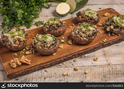 Mushroom caps stuffed with vegetables and cheese, baked in oven and garnished with a sprig of parsley. Mushroom appetizer on wooden board. Closeup