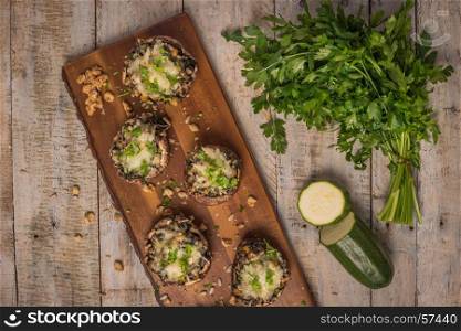 Mushroom caps stuffed with vegetables and cheese, baked in oven and garnished with a sprig of parsley. Mushroom appetizer on wooden board. Closeup