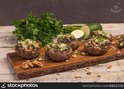 Mushroom caps stuffed with vegetables and cheese, baked in oven and garnished with a sprig of parsley. Mushroom appetizer on wooden board. Closeup