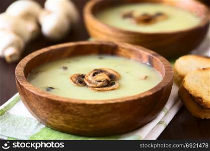 Mushroom cream soup garnished with roasted mushroom slices served in wooden bowls, photographed with natural light (Selective Focus, Focus on the front of the top mushroom slice on the first soup). Mushroom Cream Soup