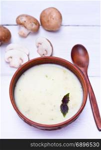 mushroom cream soup in a brown round plate with a wooden spoon on a white table