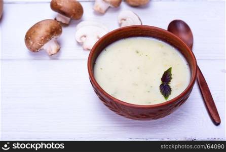 Mushroom creamy soup in a clay brown plate with a wooden spoon on a white table, empty space on the left